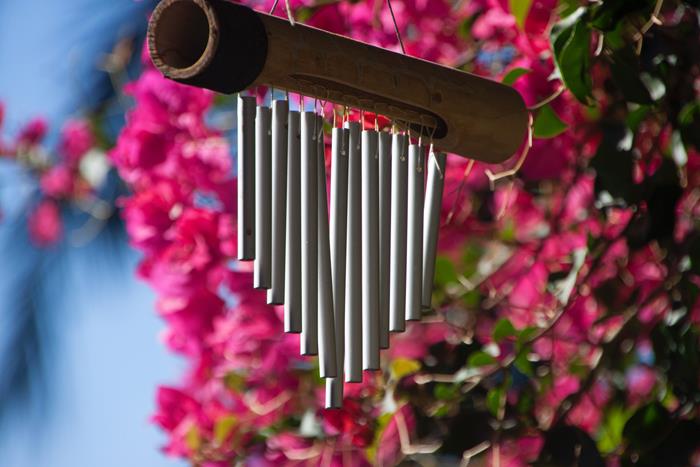 Triangle shaped wind chime set against a background of pink flowers